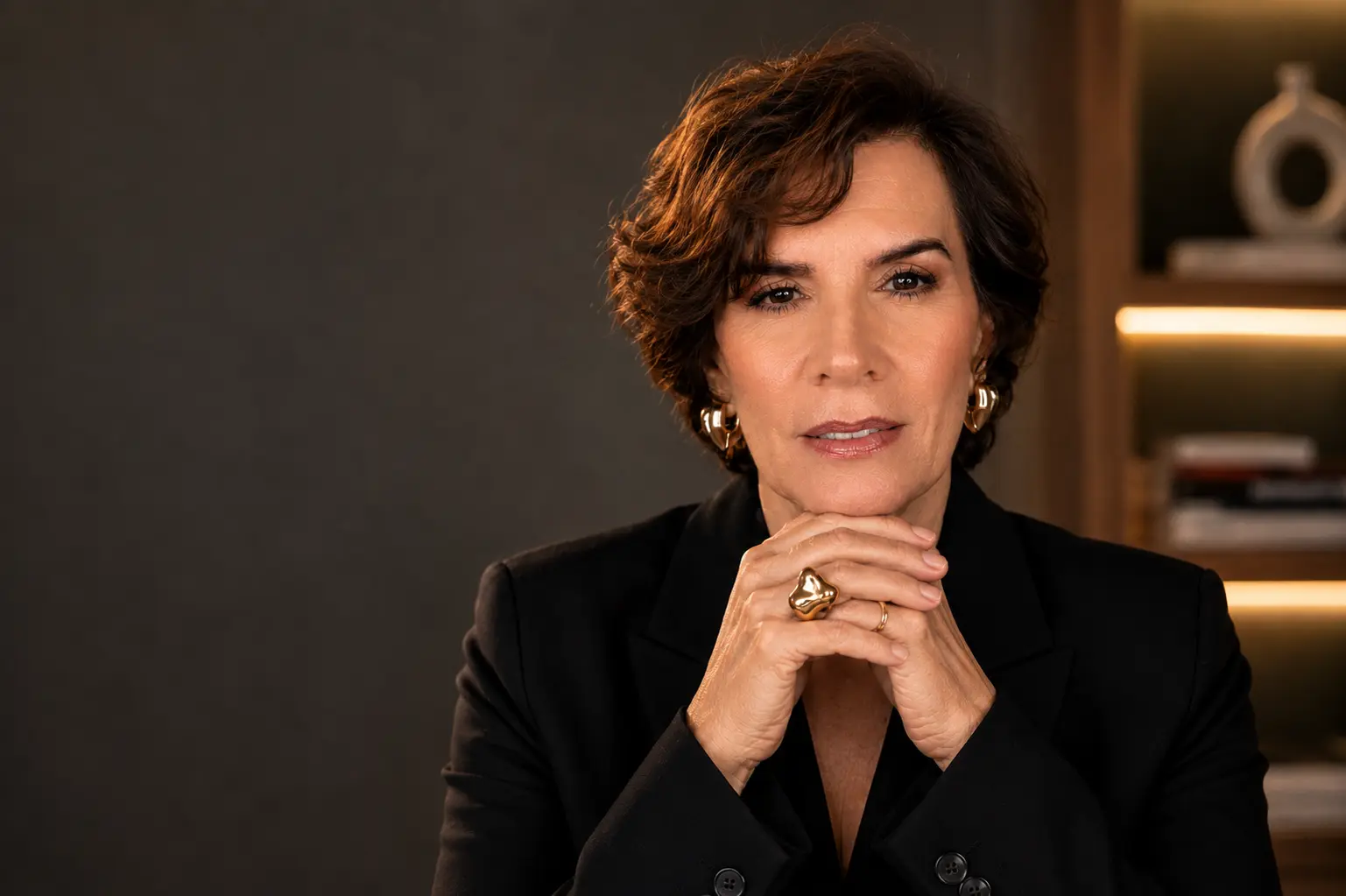 Lisiane Brito em retrato de estúdio, blazer preto, mãos apoiadas sob o queixo