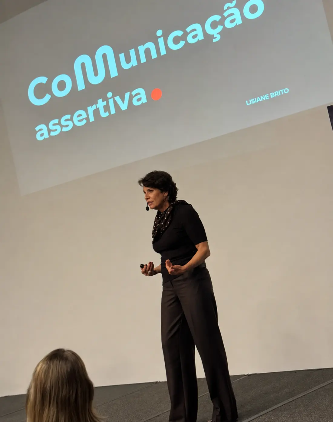 Lisiane Brito no palco, diante do telão com o título Comunicação assertiva